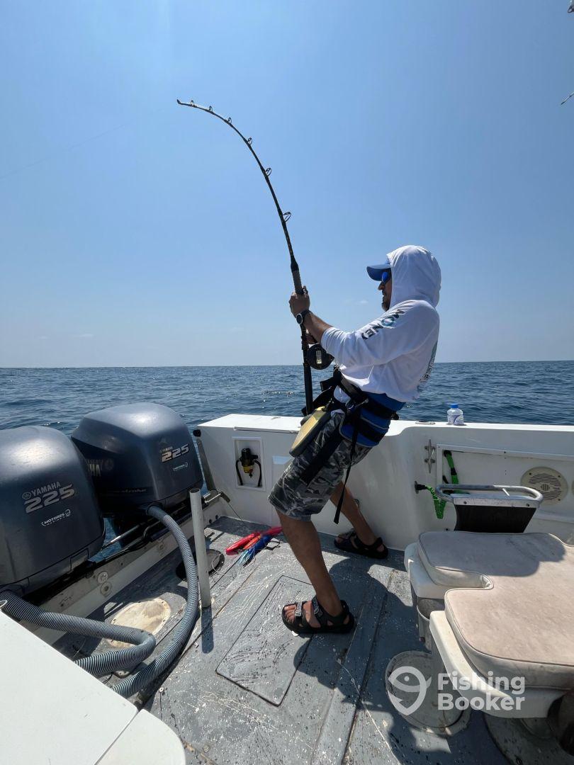 An angler actively reeling in a catch while fishing on a boat in open water, showcasing the excitement of deep-sea fishing.