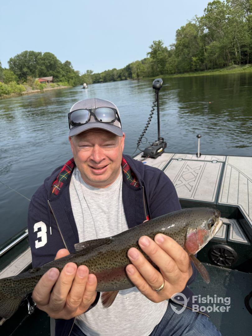 An angler proudly displaying a Rainbow Trout while fishing on a serene river, surrounded by lush greenery.