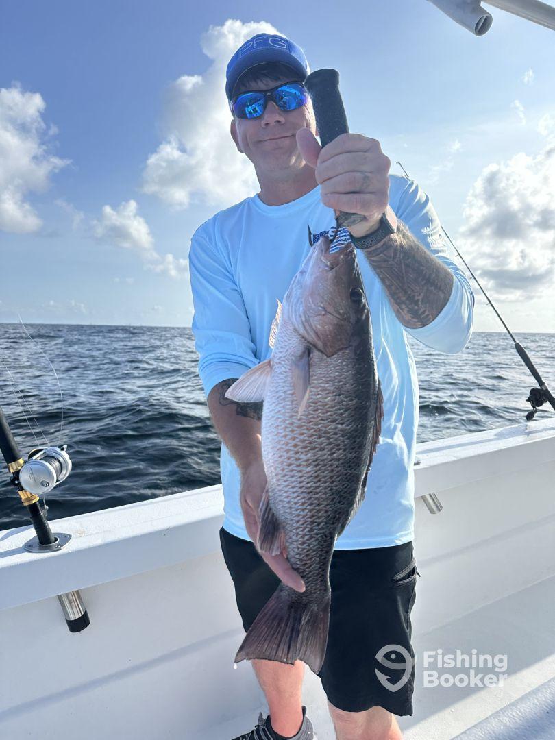 Angler proudly displaying a large Snapper while fishing offshore, showcasing a beautiful day on the water.