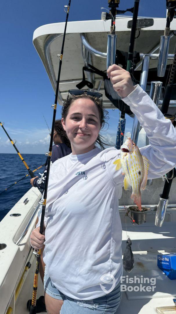 A young angler proudly displaying a colorful Mutton Snapper while fishing on a boat in open waters.