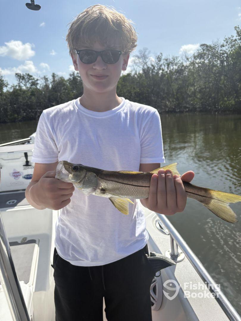 A young angler proudly displaying a Snook while fishing from a boat in a scenic coastal environment.