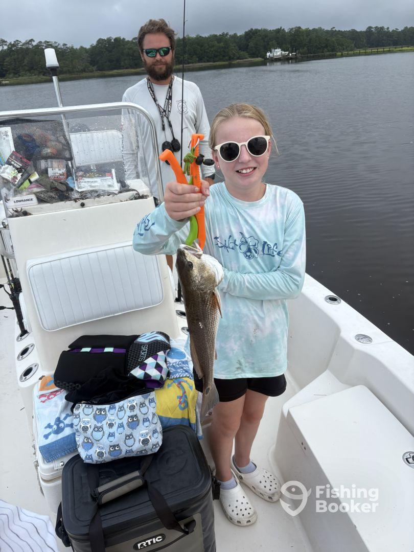 A young angler proudly displaying a caught fish while fishing on a boat in a calm waterway, showcasing a fun family fishing experience.
