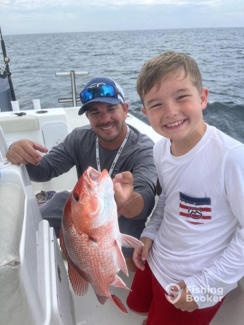 A young angler proudly displays a large Red Snapper while fishing on a boat, enjoying a memorable day on the water.
