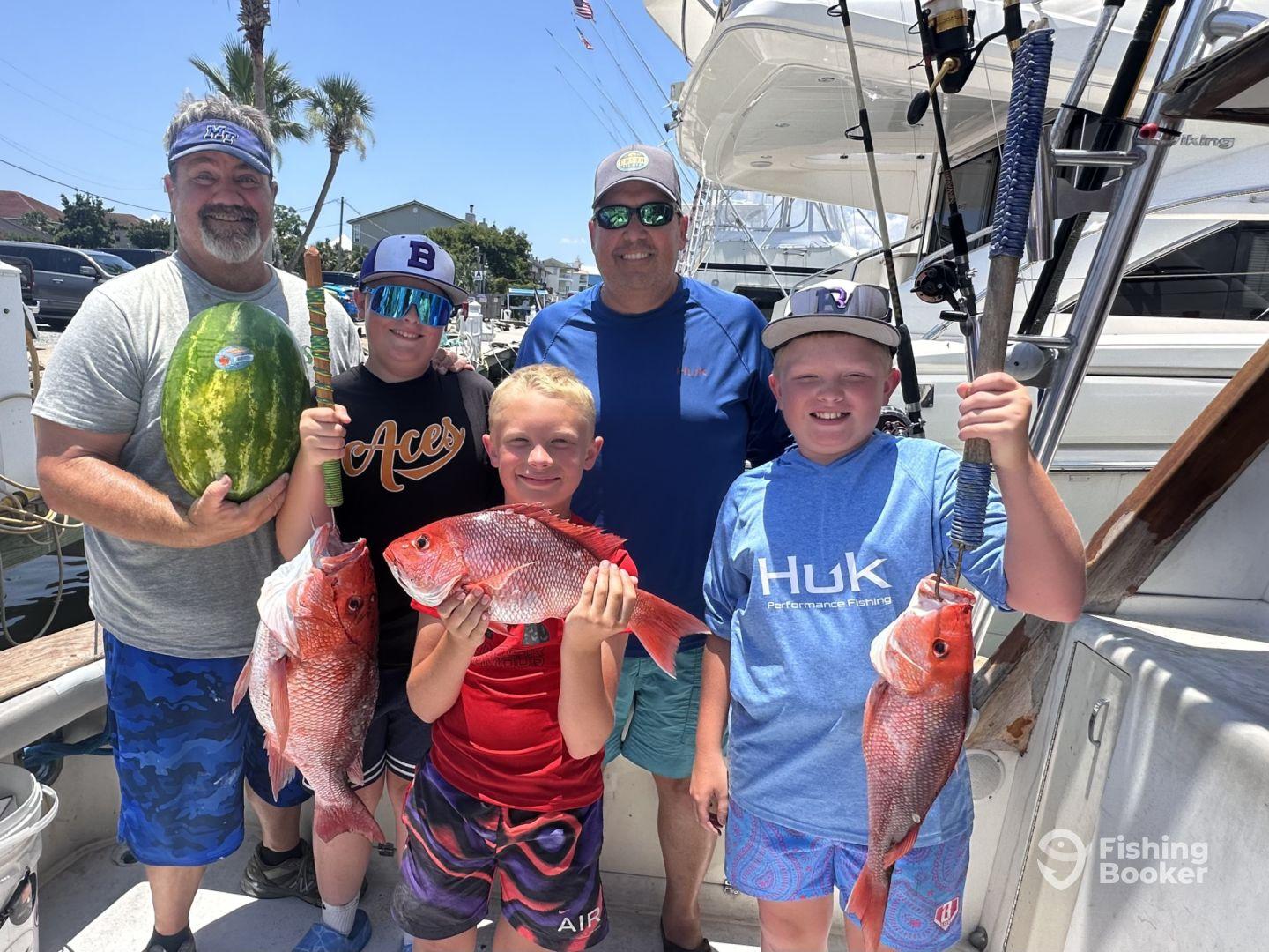 A family of young anglers proudly displaying their catch of Red Snapper while enjoying a sunny day on the water.