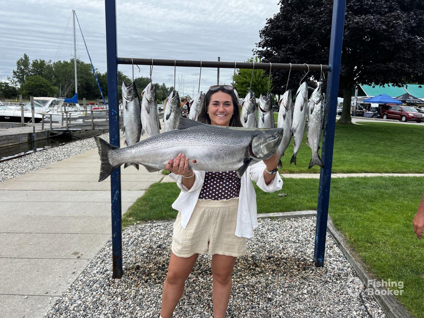 A proud angler displaying a large Salmon alongside a catch of multiple fish at the marina after a successful fishing trip.