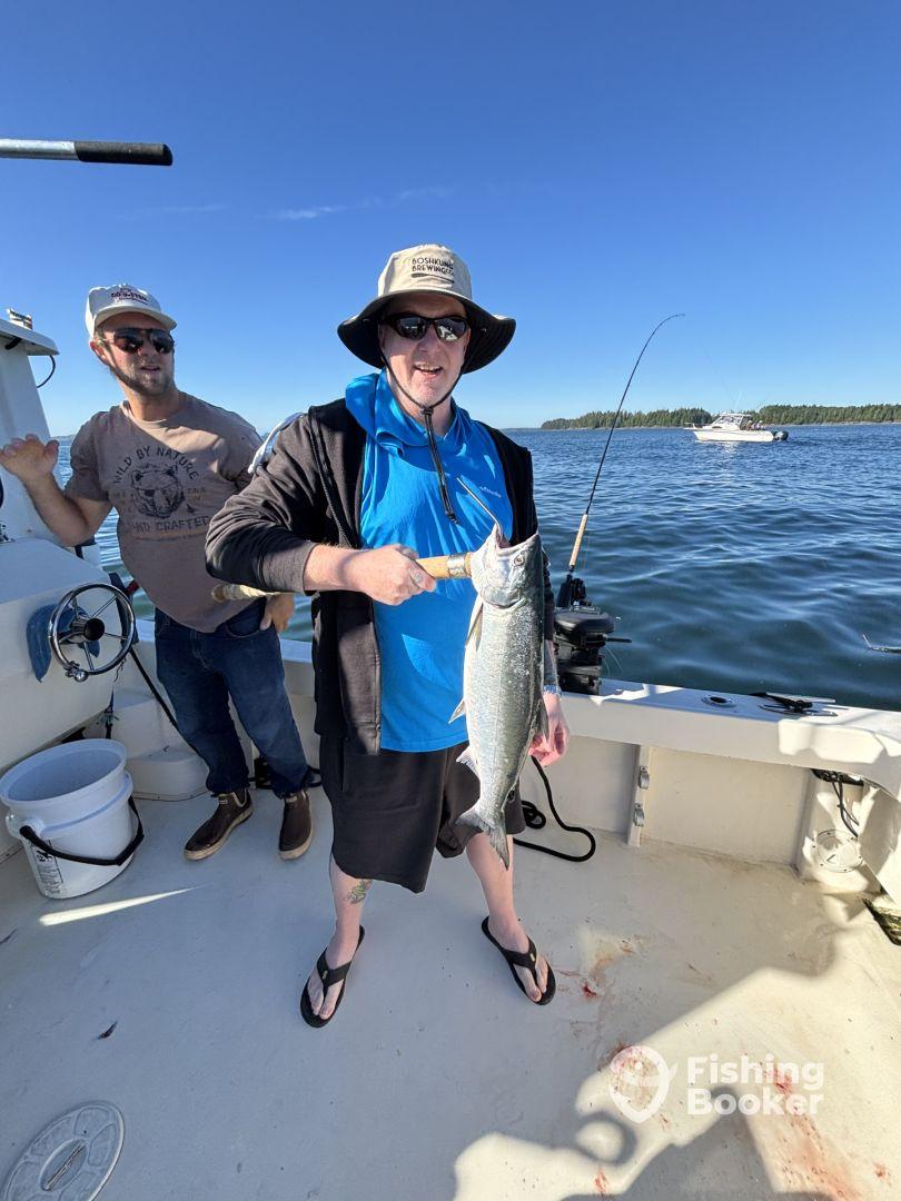 Angler proudly displaying a large fish on a boat during a sunny day fishing trip, with another person in the background.