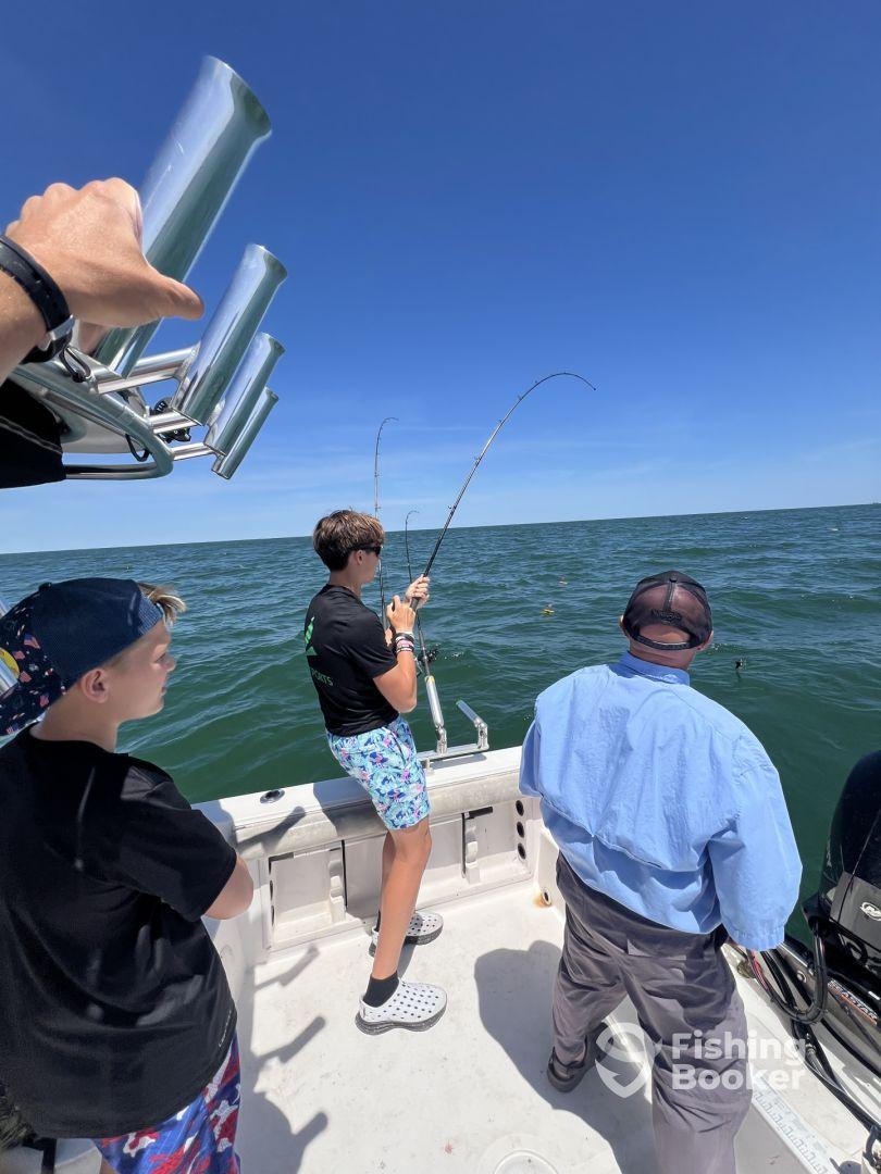 Two young anglers actively reeling in fish while fishing from a boat in clear blue waters, showcasing an exciting day on the water.