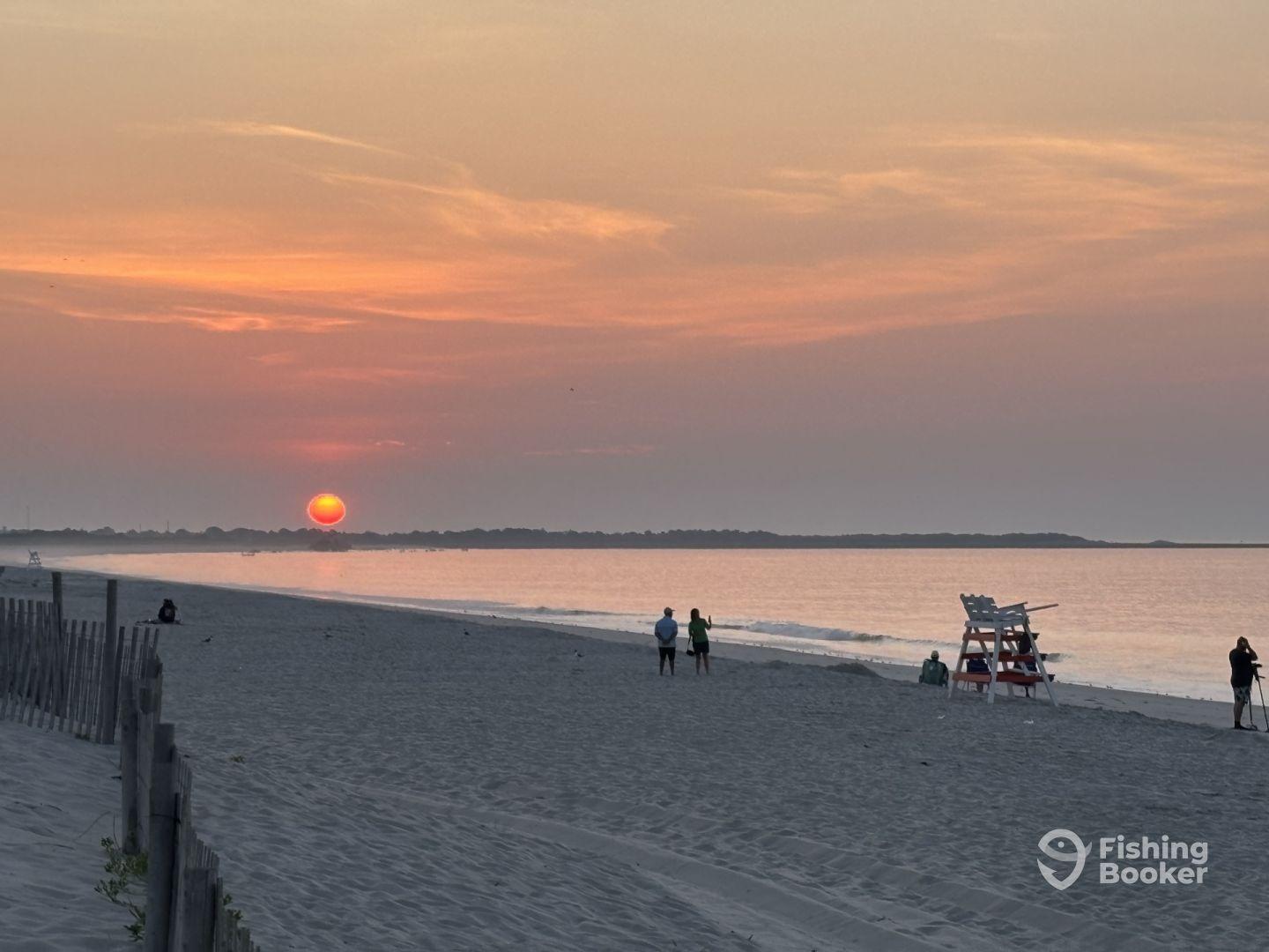 A serene beach sunset scene with people walking along the shore, capturing the tranquil atmosphere of the evening.
