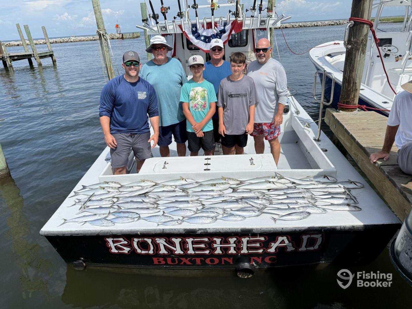 A group of anglers proudly posing with their catch of Spanish Mackerel aboard the Bonehead in Buxton, NC, showcasing a successful fishing trip.