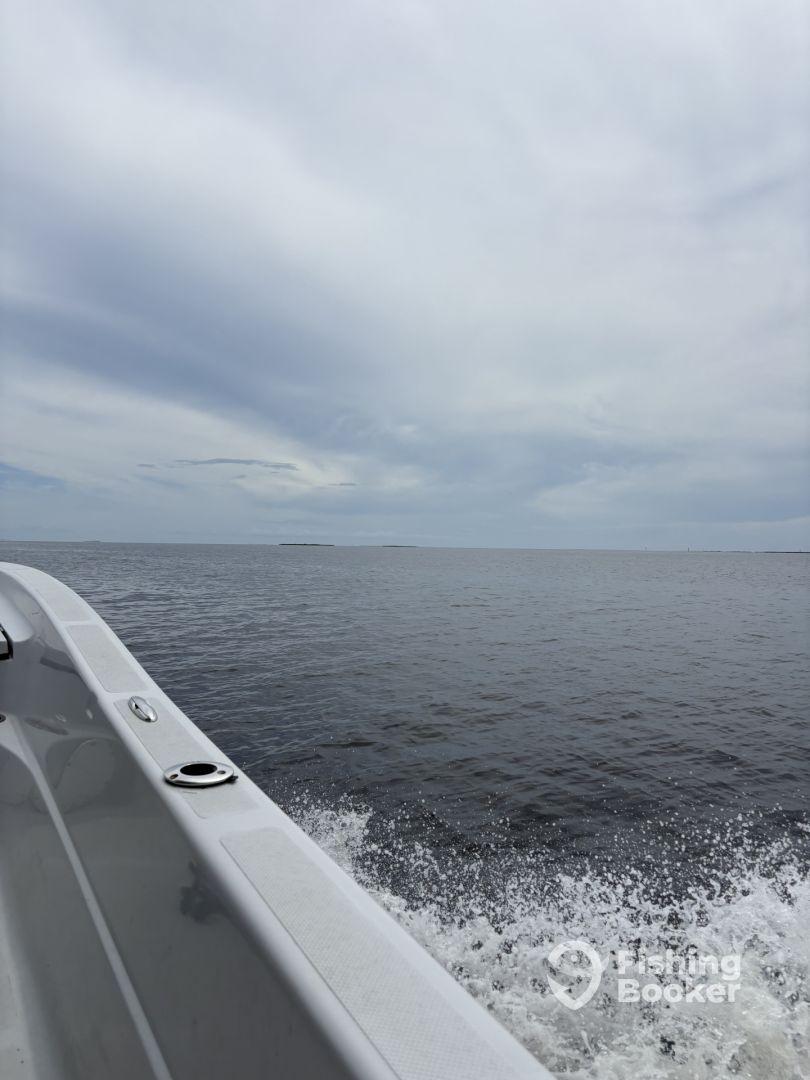 A scenic view of the boat's side as it navigates through calm waters, showcasing the expansive ocean and cloudy sky.