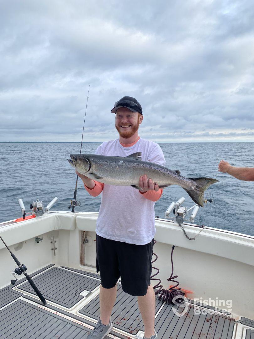 Angler proudly displaying a large Lake Trout while fishing on a boat in open water.