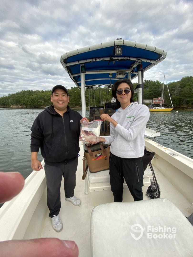 Two anglers on a boat proudly displaying their catch, a fish in a bag, while enjoying a day on the water.
