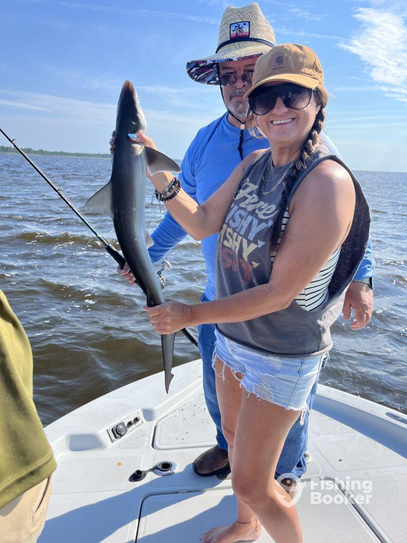 Two anglers proudly displaying a caught shark while fishing on a sunny day, showcasing the excitement of a successful outing.