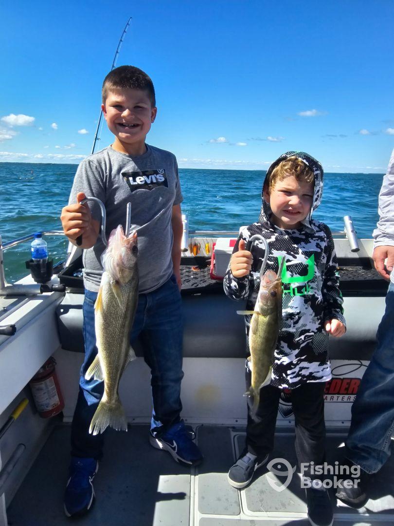 Two young anglers proudly displaying their Walleye catches aboard a fishing charter, enjoying a sunny day on the water.