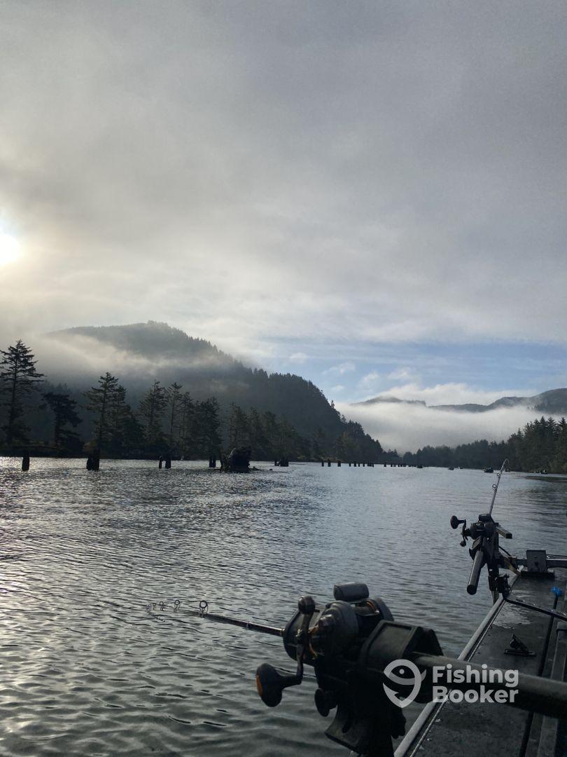A serene view of a fishing boat on a calm river, surrounded by misty mountains and trees, ideal for a peaceful fishing experience.