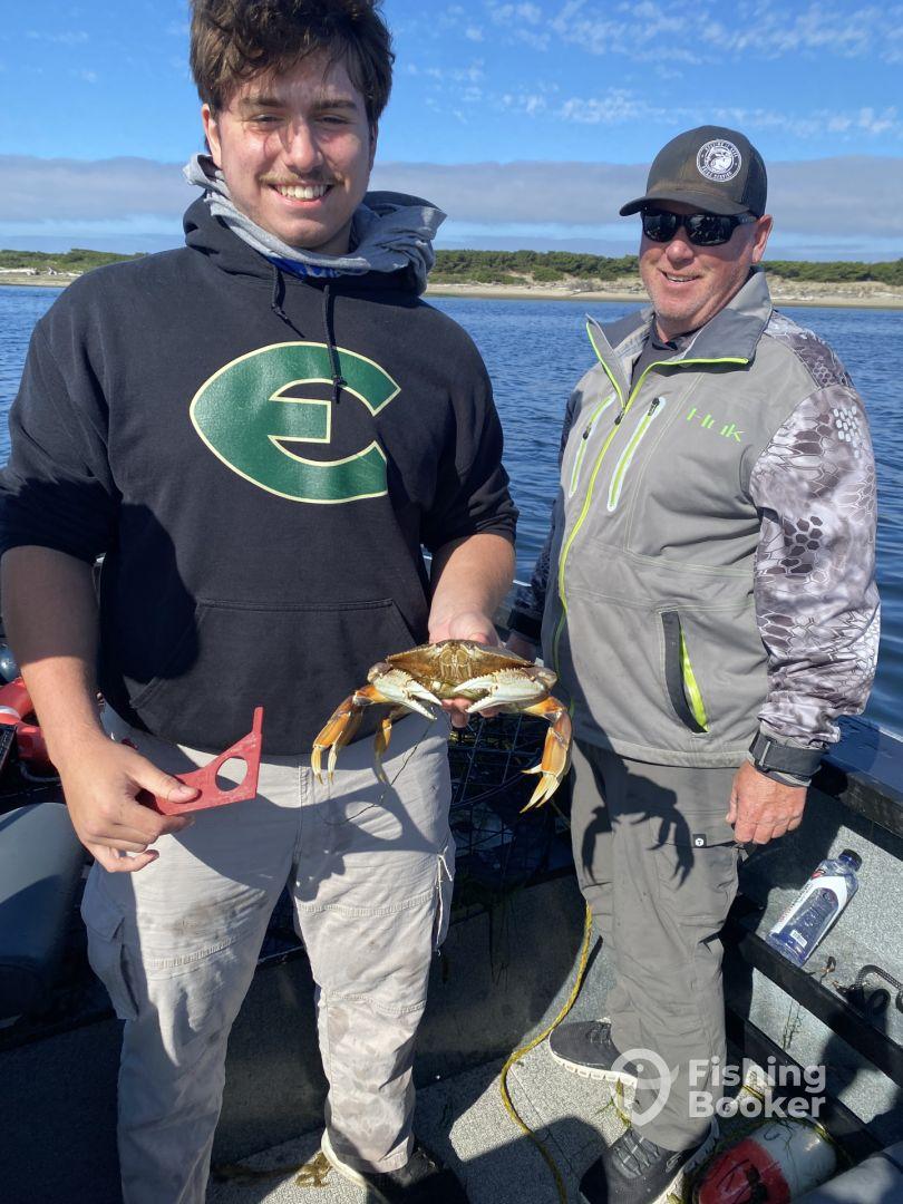 Two anglers on a boat proudly displaying a freshly caught Dungeness crab, showcasing a successful day of crabbing in a coastal environment.