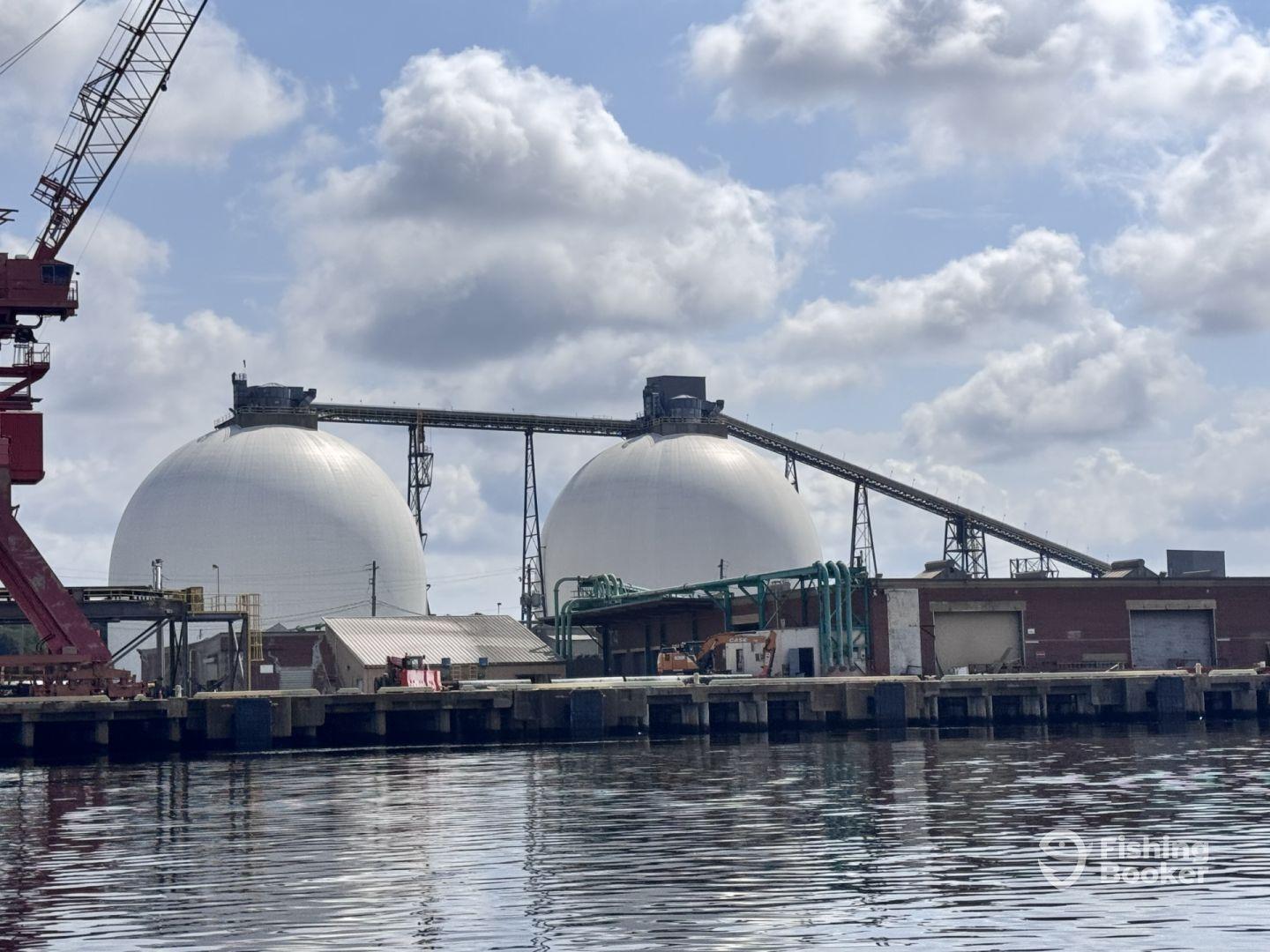 An industrial scene featuring large storage domes and a crane, likely part of a port facility.