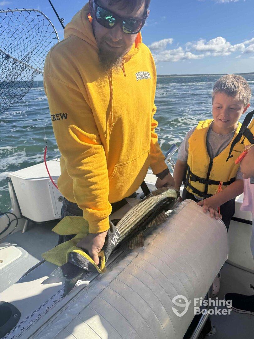 An adult and two young anglers measuring a large fish on a boat, showcasing a family-friendly fishing experience.