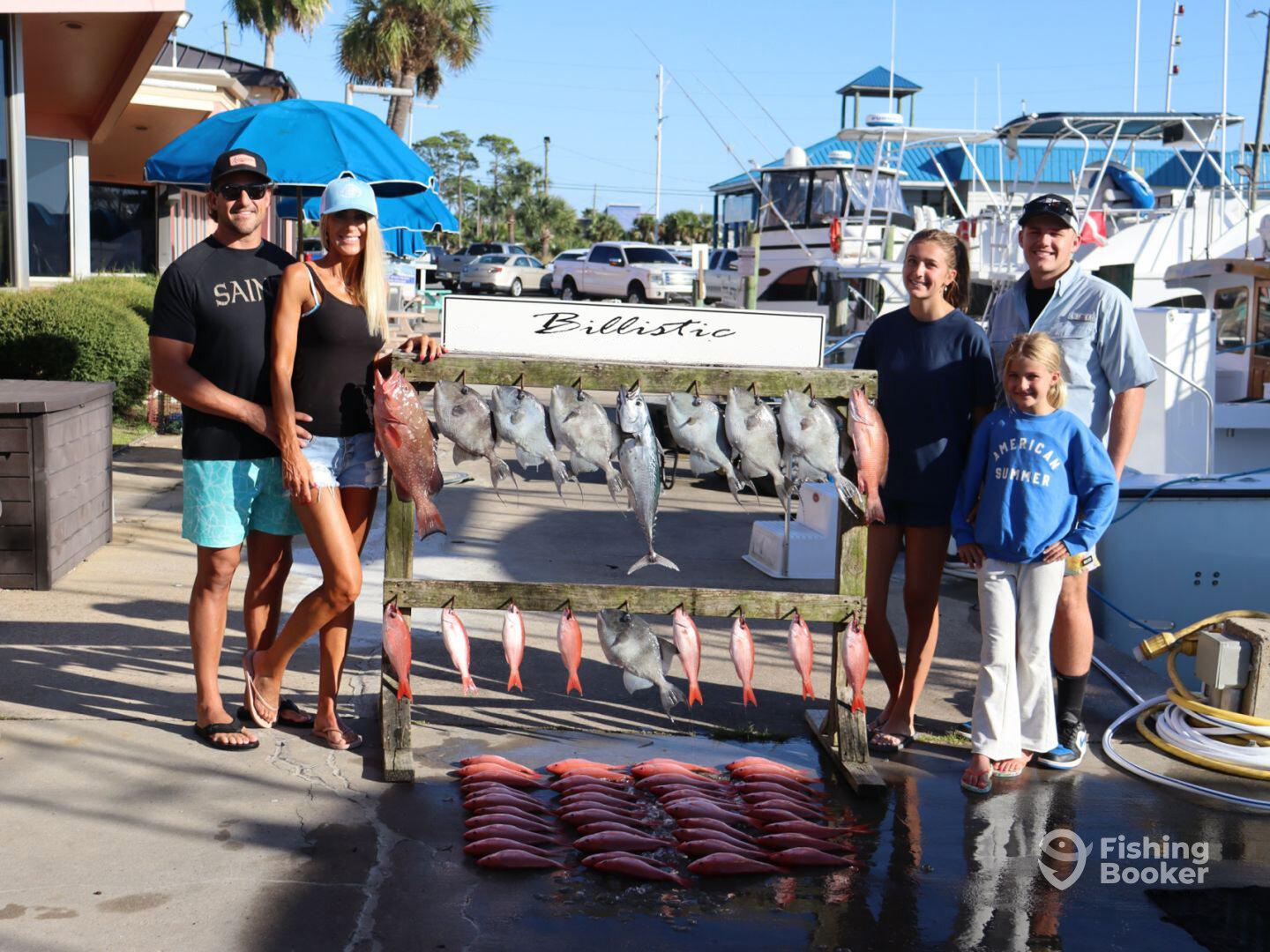 A family proudly displays their catch of the day, featuring various species of fish arranged on a catch board at the marina.