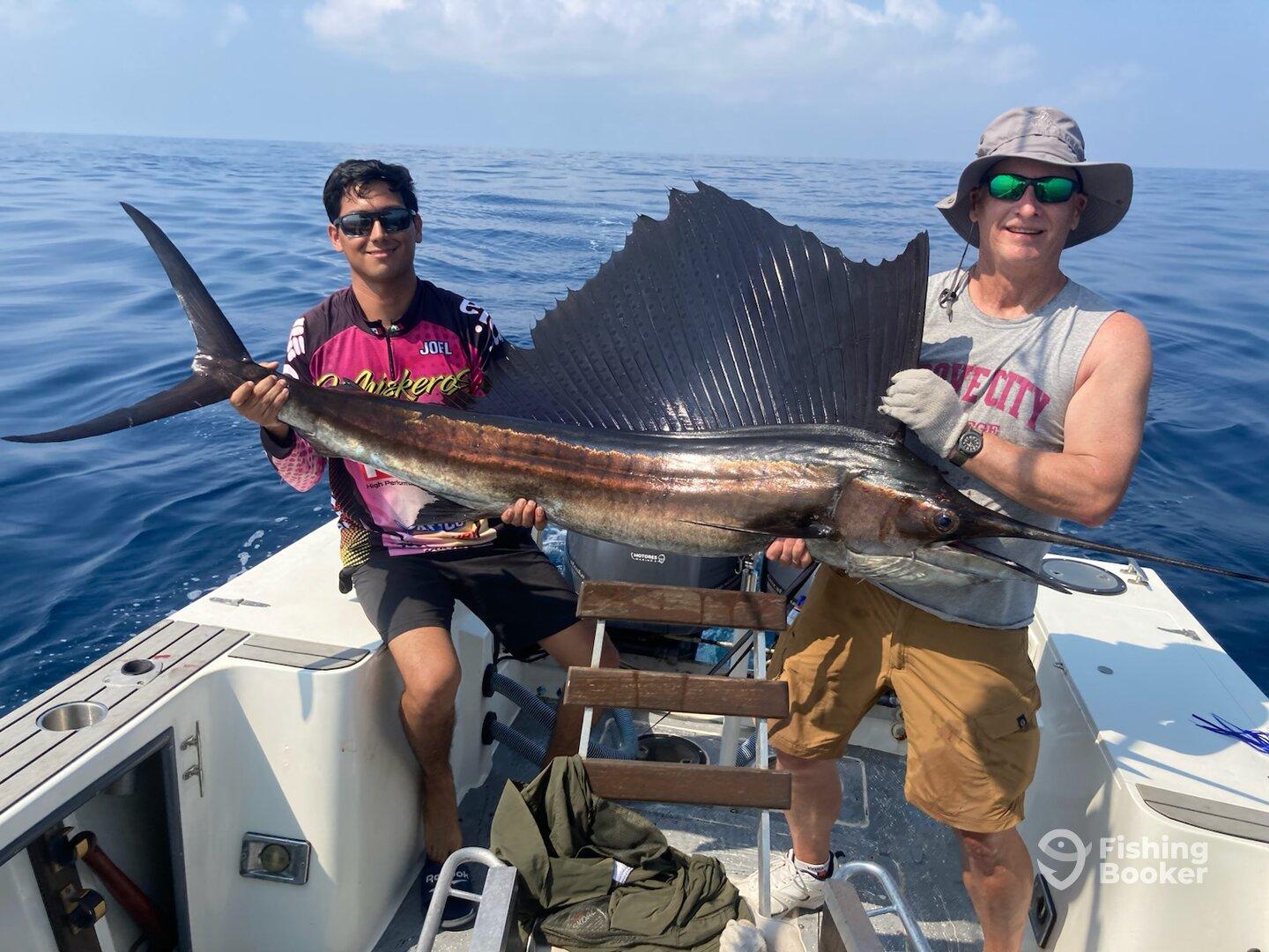 Two anglers proudly displaying a large Sailfish aboard a boat in open waters, showcasing a successful deep-sea fishing trip.