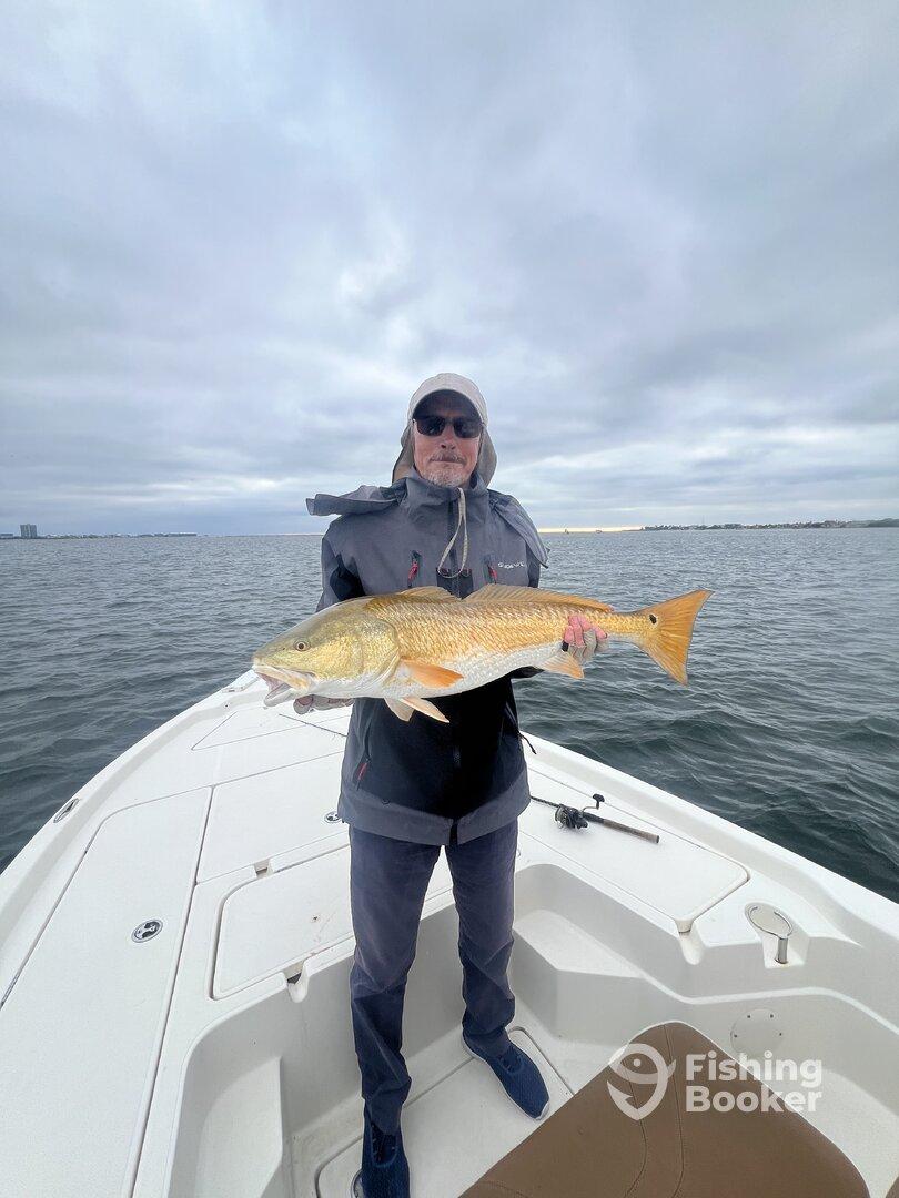 An angler proudly displaying a large Redfish while fishing on a boat in a coastal waterway.