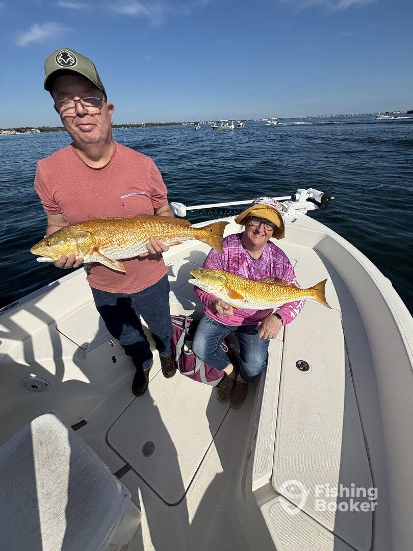 Two anglers proudly displaying their catches of Redfish while enjoying a sunny day on the water.