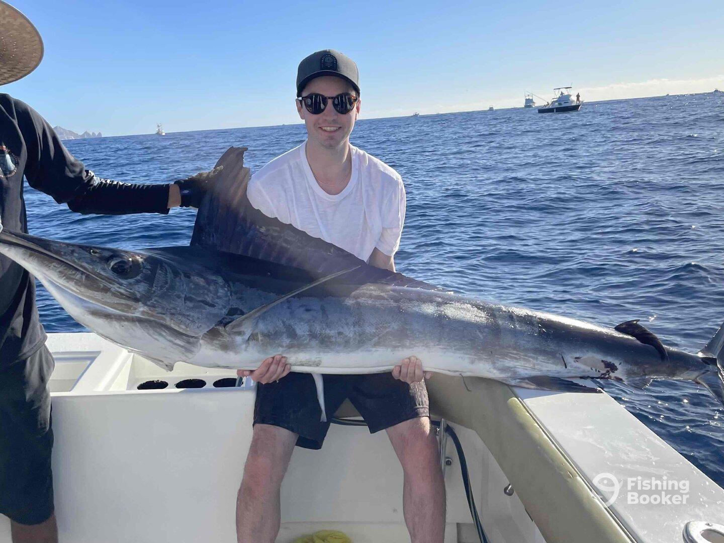 An angler proudly displaying a large Marlin aboard a fishing boat, showcasing a successful deep-sea fishing trip.