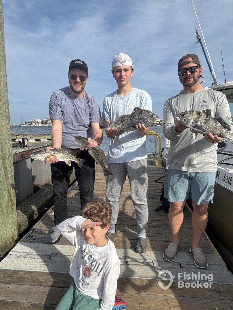 A family group proudly displaying their catch of Black Drum and Redfish at the dock after a successful fishing trip.