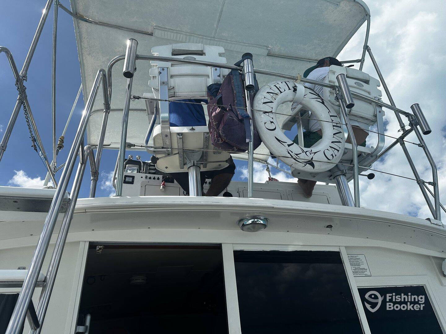 View of the boat's upper deck with crew members at the helm, showcasing the Gannet boat's features against a clear blue sky.