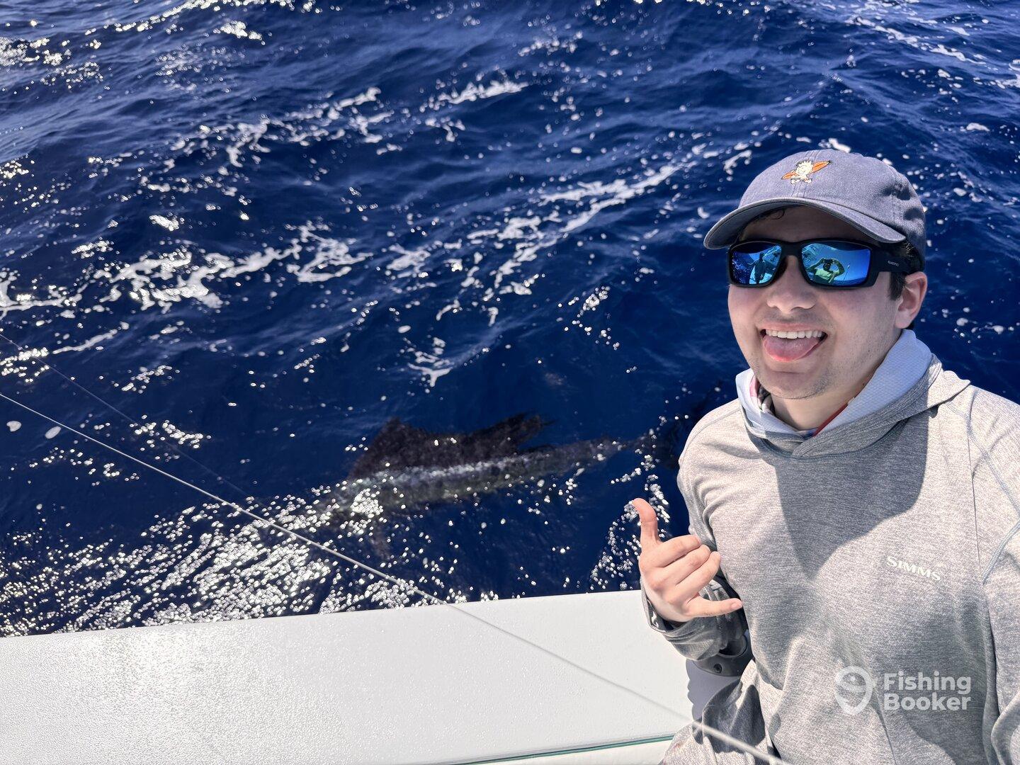 A young angler enjoying a fun moment while fishing offshore, with a glimpse of a fish in the water behind him.