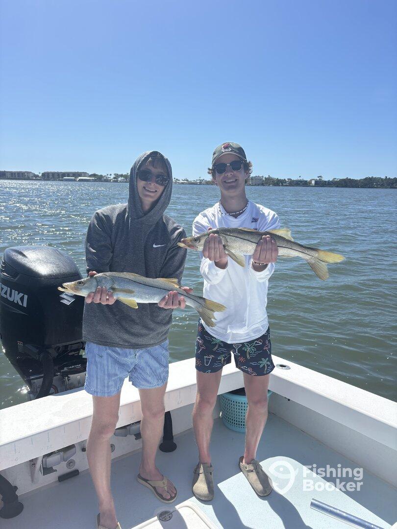Two young anglers proudly displaying their catch of Snook while enjoying a sunny day on the water.