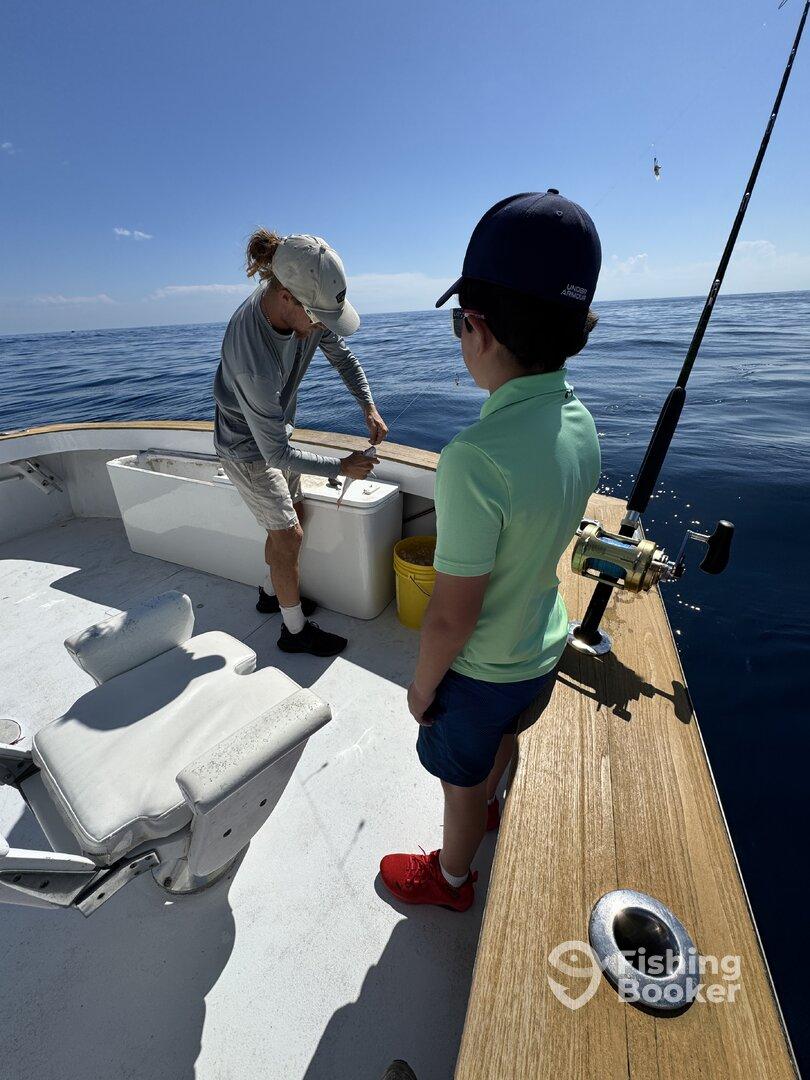 A young boy watches intently as an adult prepares fishing gear on a boat, enjoying a day out on the open water.