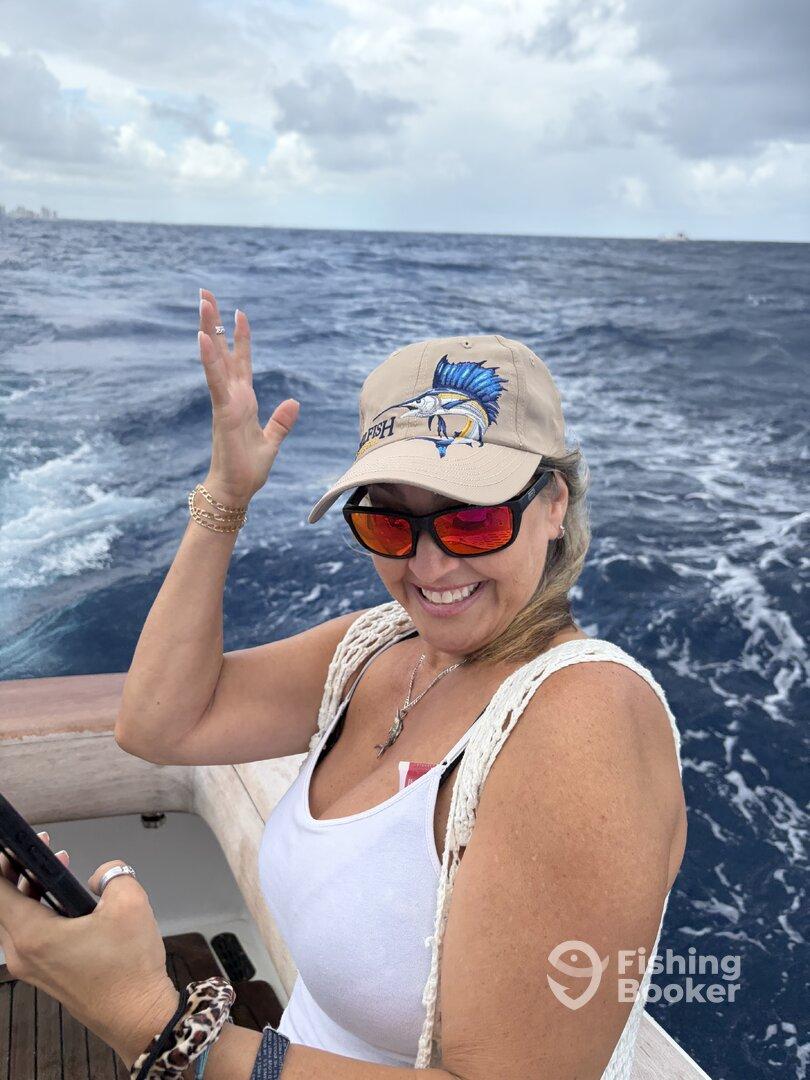 A smiling angler enjoying a day on the water, wearing a fishing hat and sunglasses, with the ocean in the background.