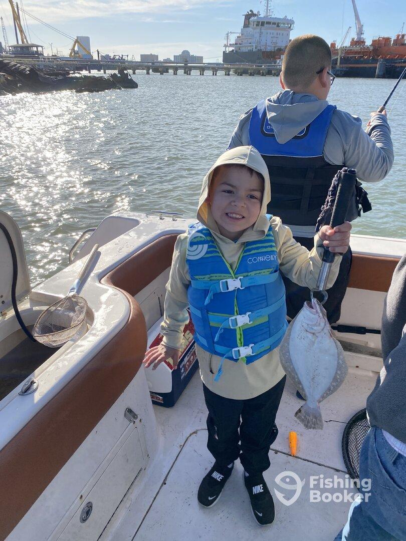 A young angler proudly holding a Flounder while fishing from a boat, showcasing a fun family outing.