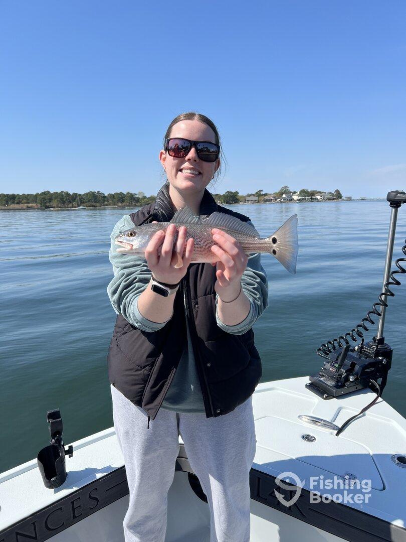 A young woman proudly displaying a freshly caught Redfish while enjoying a day on the water.