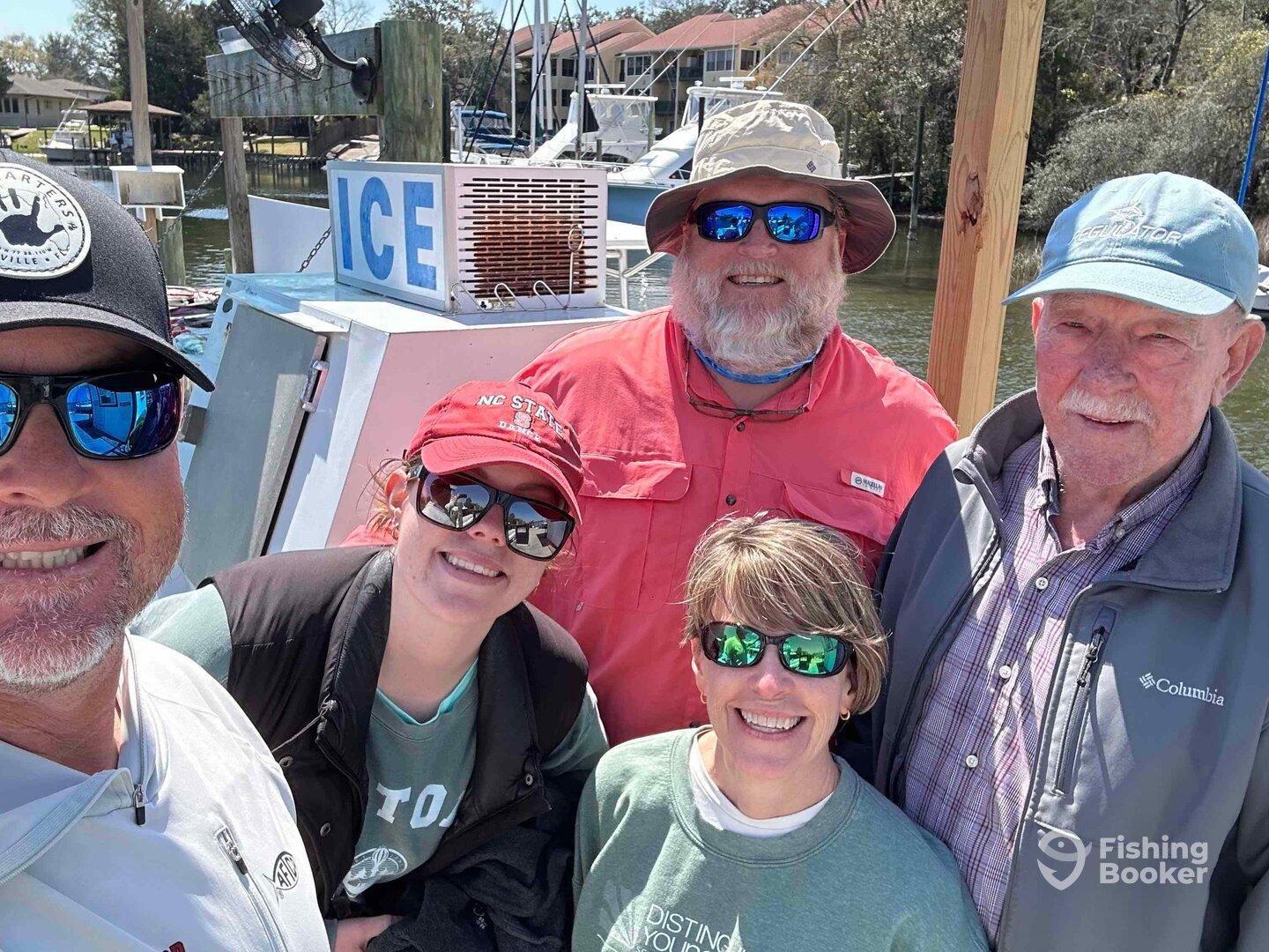 A cheerful group of anglers posing for a selfie on the dock, with a boat in the background, showcasing a fun day of fishing.