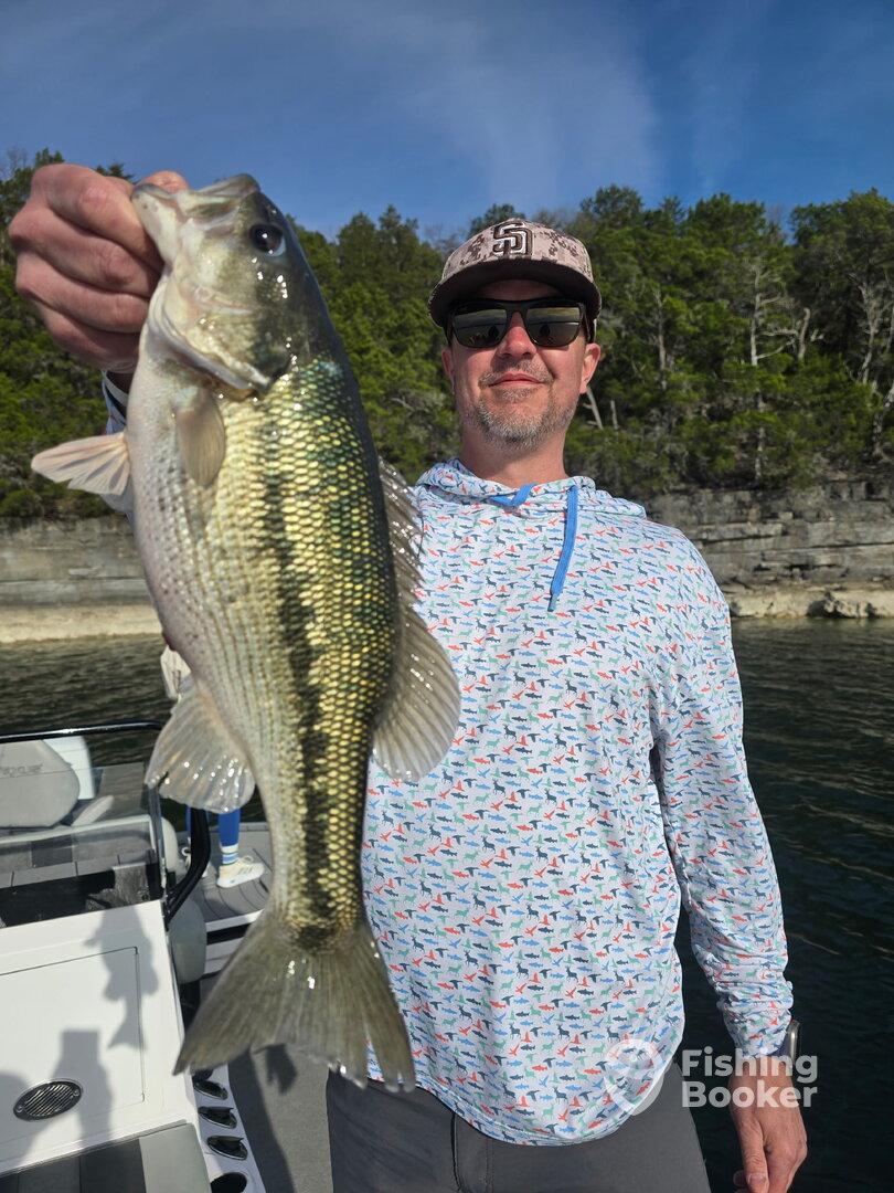 Angler proudly displaying a large Largemouth Bass while fishing on a scenic lake.