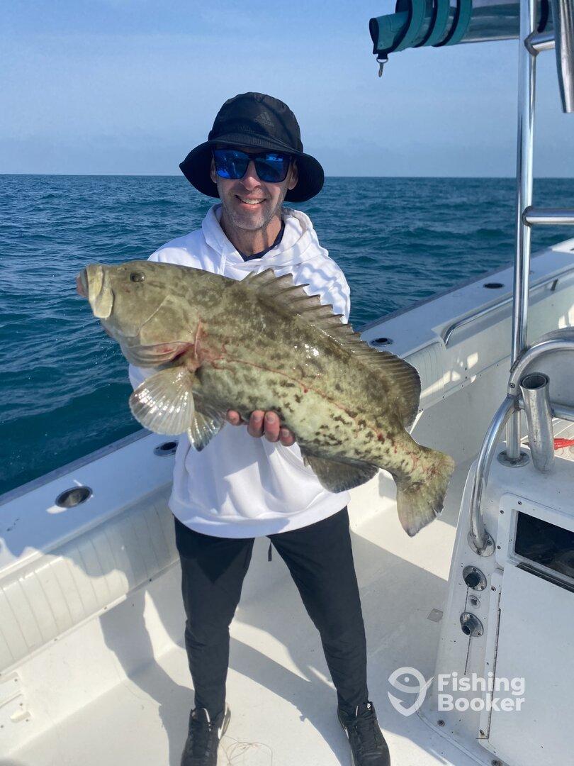 Angler proudly displaying a large Goliath Grouper while fishing on a boat in open waters.