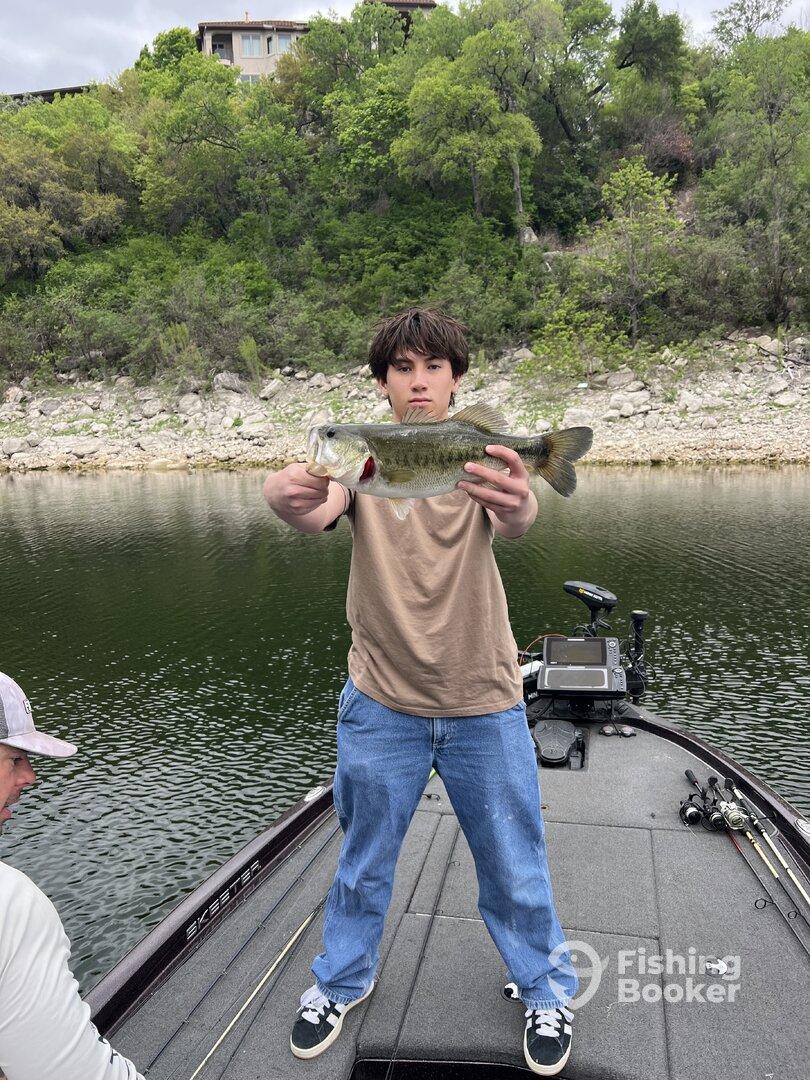 A young angler proudly displaying a large Largemouth Bass while fishing from a Skeeter boat on a serene lake.