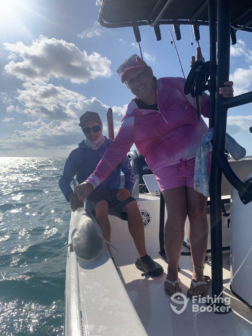 Two anglers enjoying a sunny day on the water, proudly displaying a caught shark while aboard a fishing boat.