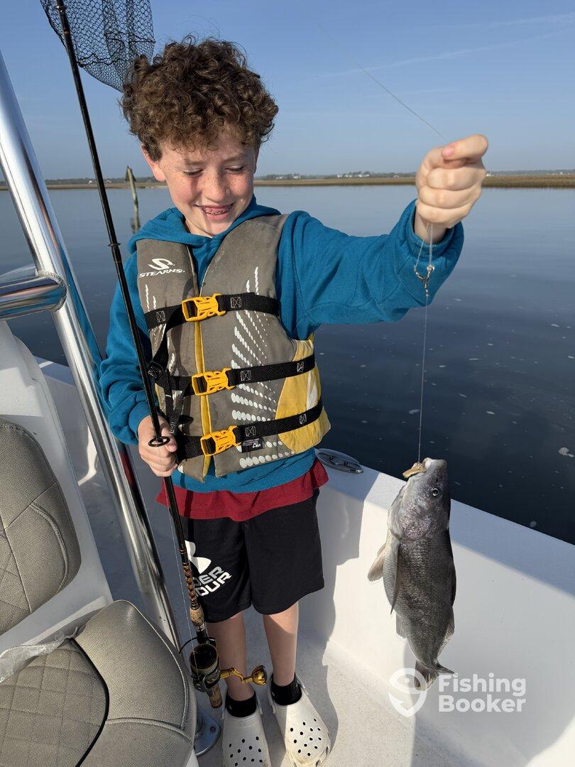 A young angler joyfully displaying a freshly caught fish while fishing from a boat in calm waters.