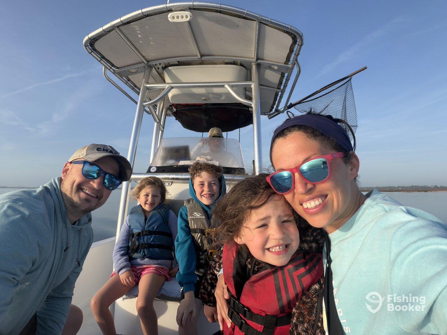 A joyful family of four enjoying a sunny day on a fishing boat, with kids wearing life jackets and smiling for the camera.