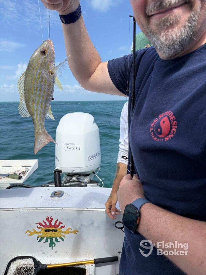 Angler proudly displaying a freshly caught Yellowtail Snapper while fishing on a boat in clear waters.