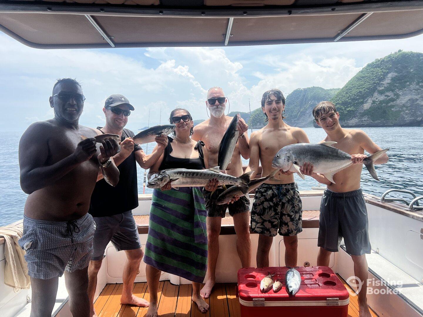 A group of anglers proudly displaying their catch, including a large Gray Snapper and other species, aboard a fishing boat in a scenic coastal setting.