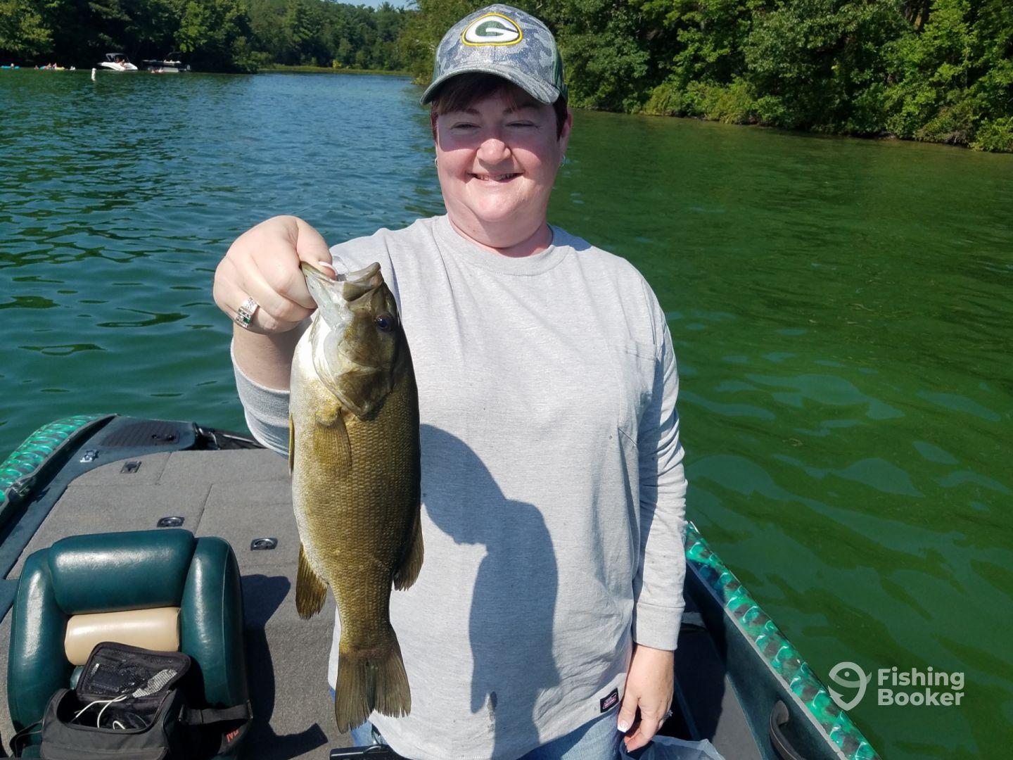 An angler proudly displaying a healthy Smallmouth Bass while fishing on a serene lake surrounded by lush greenery.