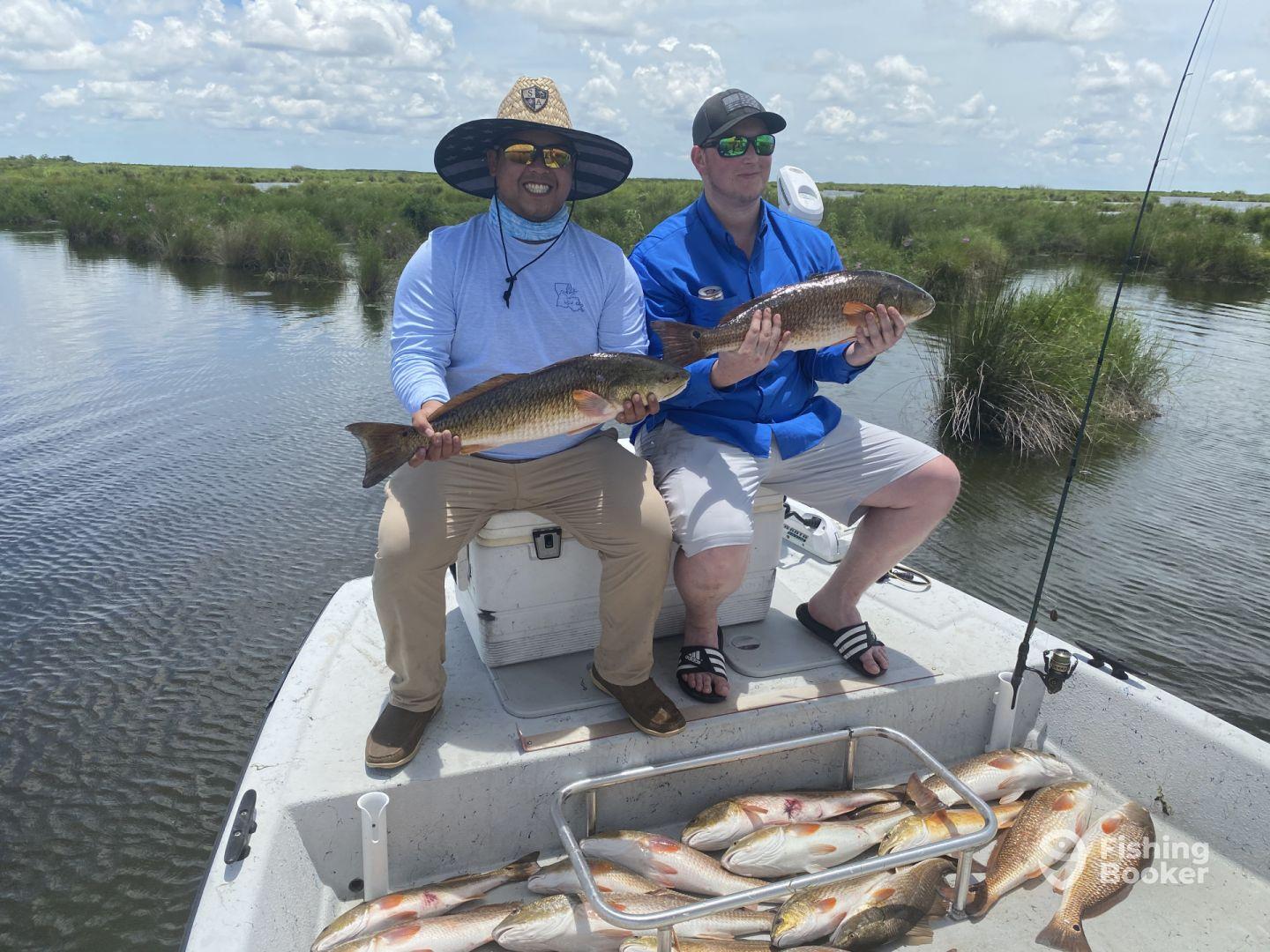 Two anglers proudly displaying their catches of Redfish while fishing in a scenic marsh environment.