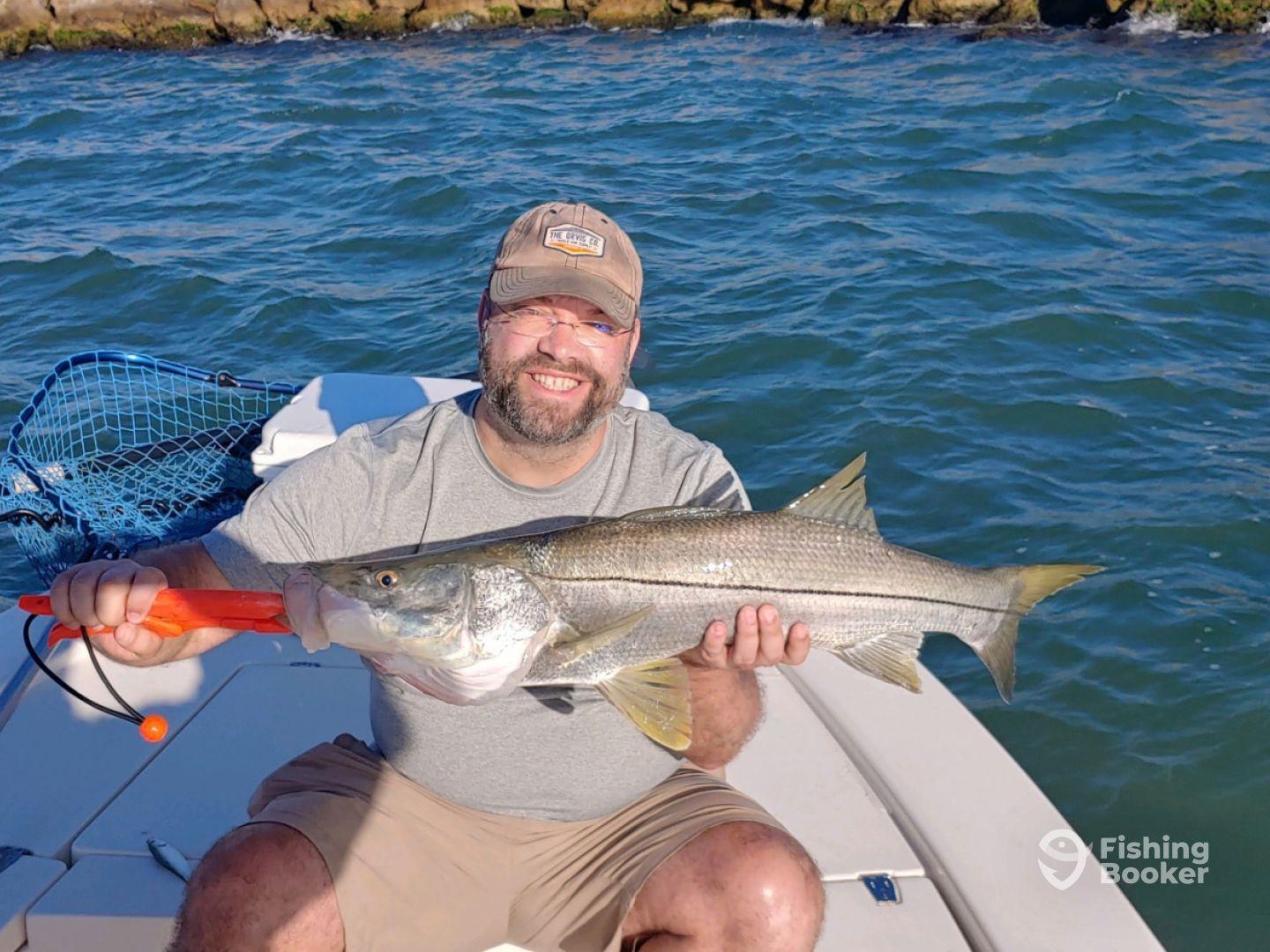 An angler proudly displaying a large Snook while fishing from a boat in a coastal environment.