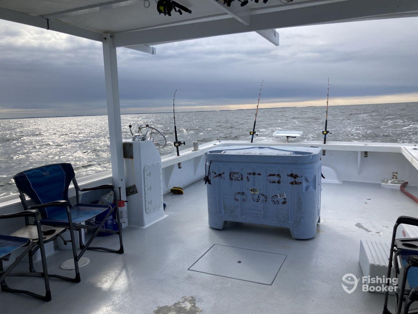 Interior view of a fishing boat showcasing seating and fishing gear, set against a backdrop of a calm sea under a cloudy sky.