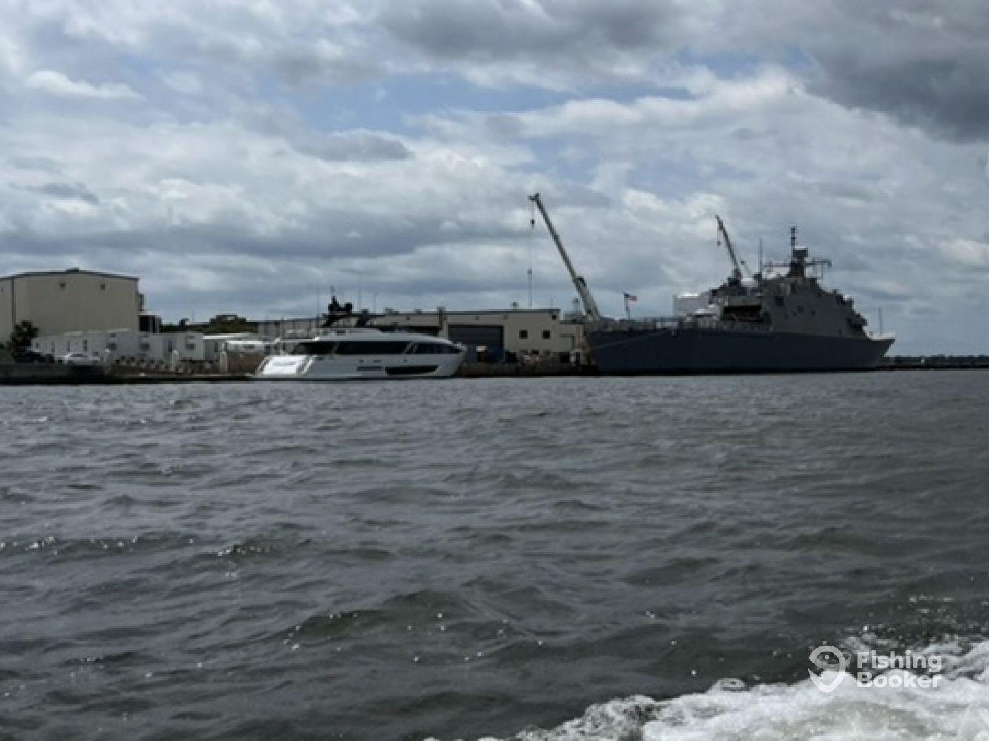 A view of two boats docked at a marina, showcasing a sleek yacht alongside a larger naval vessel under a cloudy sky.