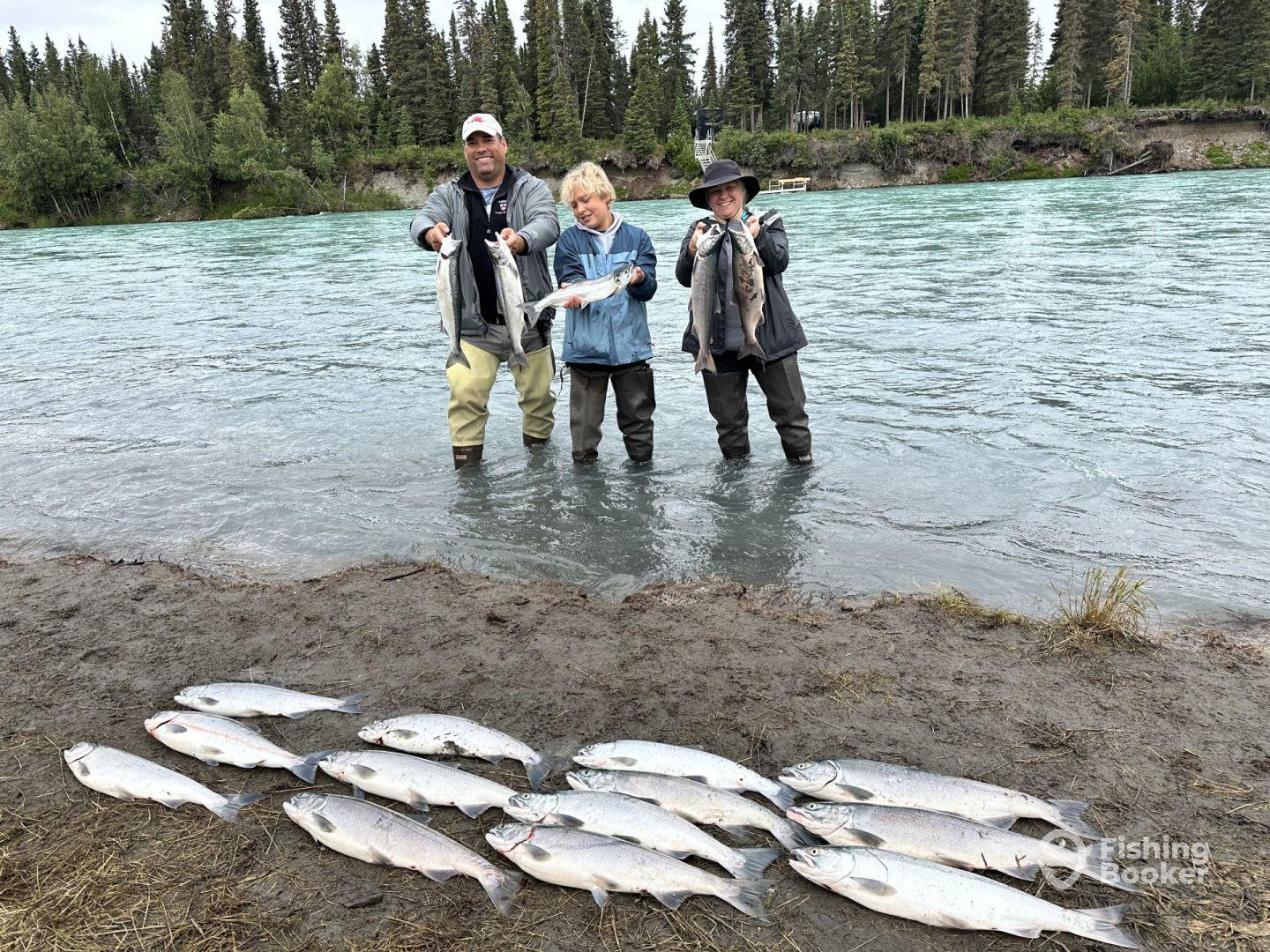A family fishing trip at a river, showcasing their catch of several Silver Salmon, with two adults and a child proudly displaying their fish.